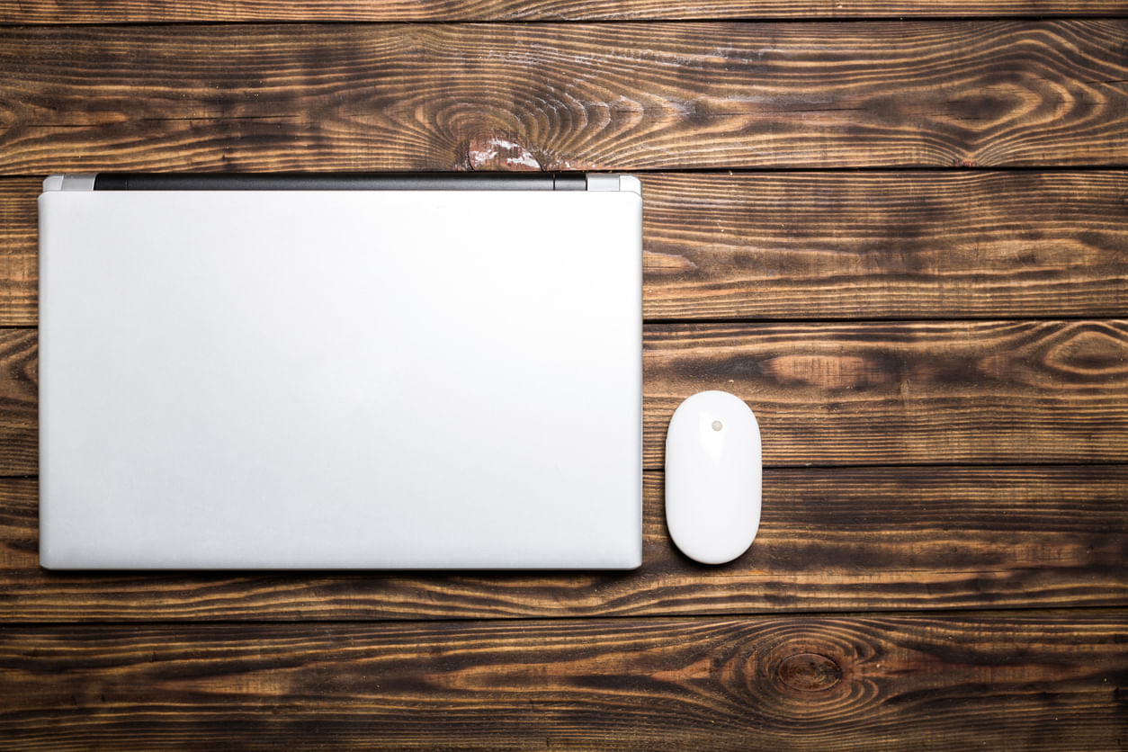 Promoções Black Friday: Vistos de cima, estão um notebook com a tela fechada e um mouse, lado a lado sobre uma superfície de madeira.