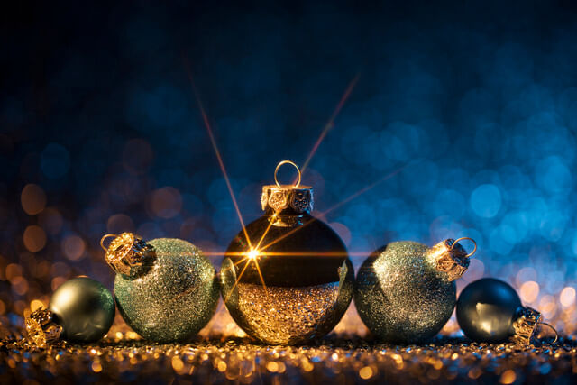 Ofertas de Natal 2018: sobre fundo azul, estão cinco bolas de Natal. Das extremidades para o centro, temos duas bolas pequenas prateadas, duas bolas médias com glitter prata e, ao centro, uma bola dourada grande refletindo um ponto de luz