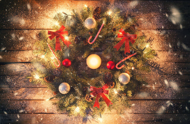 Ofertas de Natal 2018: guirlanda com folhas, laços vermelhos, bolas de Natal brilhantes, bengalas com listras brancas e vermelhas e pisca-piscas sobre uma superfície de madeira
